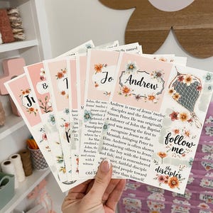 May include: A hand holds several cards with floral designs and names like "Andrew" and "John." The cards have a pink background and decorative borders. The words "follow me" and "the disciples" are also visible.