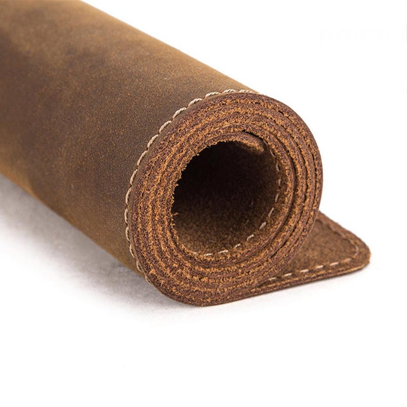 May include: Rolled-up brown leather material with visible grain and a stitched edge. The leather has a distressed appearance, suggesting a vintage or rustic aesthetic. The material is likely used for crafting or as a decorative element.