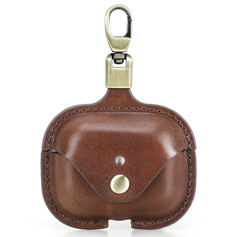 May include: Brown leather AirPod case with a brass-colored clasp and button closure. The case has a stitched border and a small flap. The top has a brass-colored clasp for attaching to a bag or keychain.