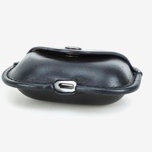 May include: A black leather case with a rounded shape and a snap closure. The case has a silver-colored metal accent on the front and a stitched border. The case is designed to hold small items.