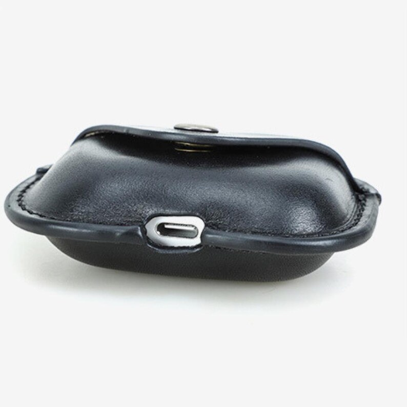 May include: A black leather case with a rounded shape and a snap closure. The case has a silver-colored metal accent on the front and a stitched border. The case is designed to hold small items.