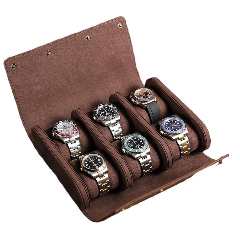 May include: A brown leather watch roll with six watches. The watches have silver and gold bands, black and blue faces, and a black rubber band. The watch roll is open, revealing the watches nestled in individual compartments.