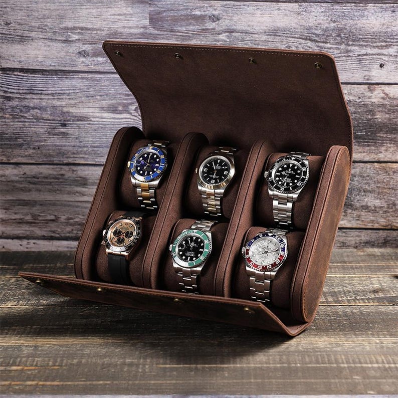 May include: A brown leather watch case with six compartments, each holding a silver wristwatch. The watches have various colored faces and bands. The case is open, revealing the watches inside.