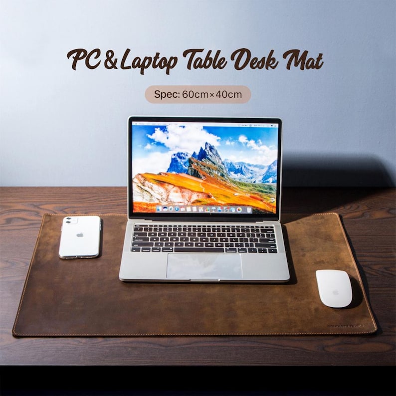 May include: A brown leather desk mat with the text "PC & Laptop Table Desk Mat" and "Spec: 60cm x 40cm". A laptop, a white mouse, and a smartphone are on the mat. The mat is on a wooden desk.