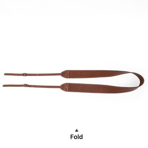 May include: A brown leather camera strap with a stitched design. The strap has adjustable sections with metal buckles and the word "Fold" printed at the bottom.