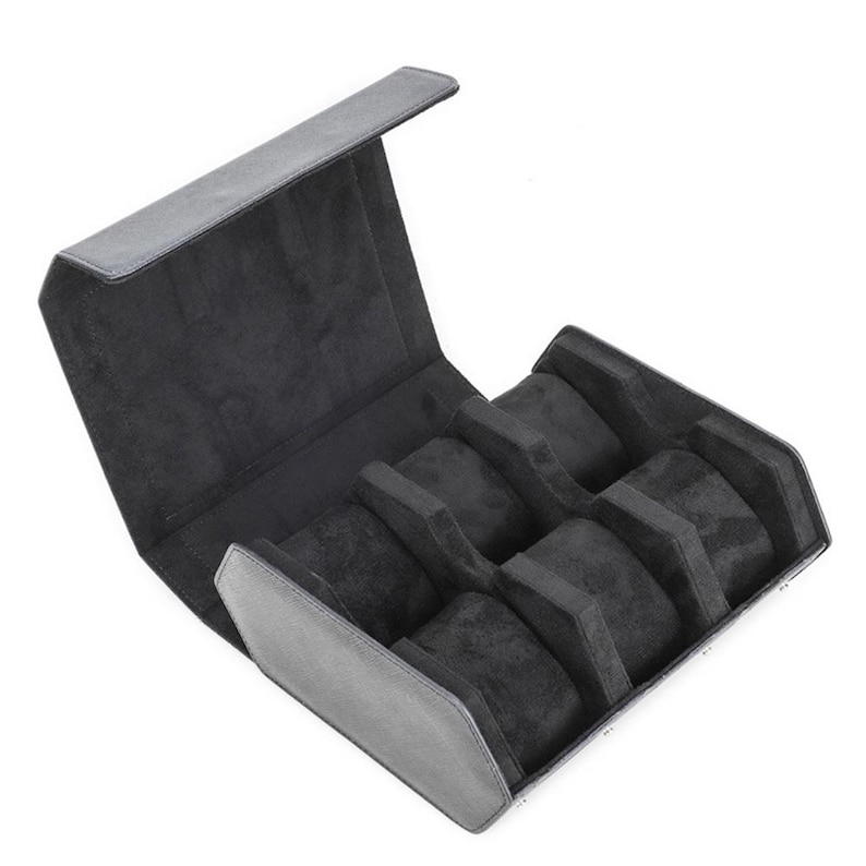 May include: A black watch case with a hinged lid, open to reveal six individual compartments. The interior is lined with a soft, dark gray material, providing a protective space for storing watches. The exterior is a smooth, dark gray.