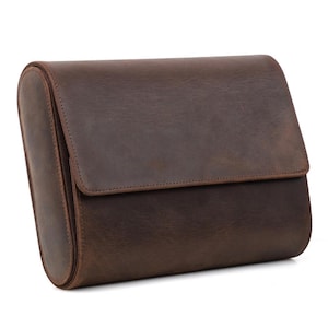 May include: A brown leather travel bag with a rectangular shape and a flap closure. The bag has a rounded side and is made of a distressed leather material. The bag is designed for travel and storage.