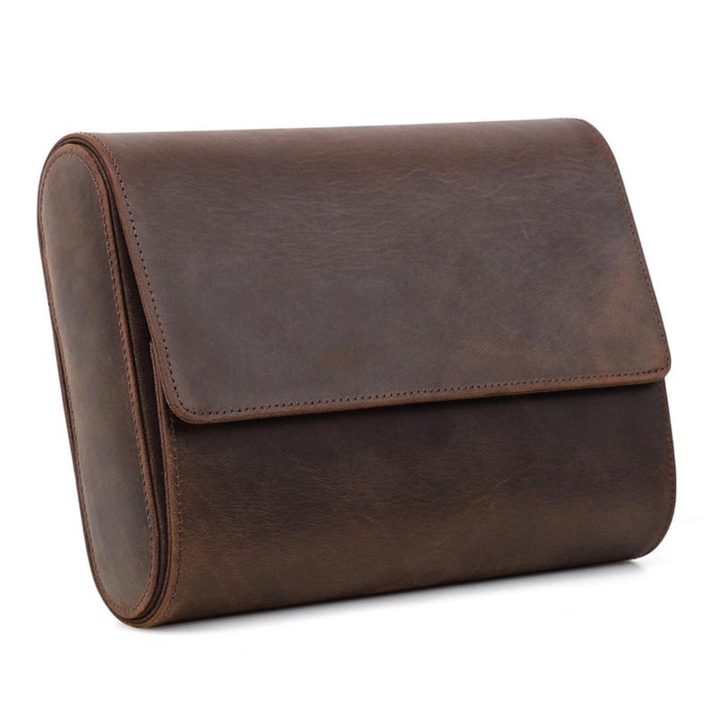 May include: A brown leather travel bag with a rectangular shape and a flap closure. The bag has a rounded side and is made of a distressed leather material. The bag is designed for travel and storage.