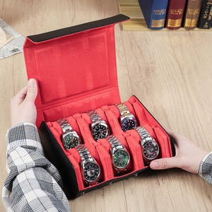May include: A black and red watch case with six silver watches. The case is open, revealing a red interior with individual slots for each watch. The watches have various colored watch faces and silver bands. The case is held by a person.