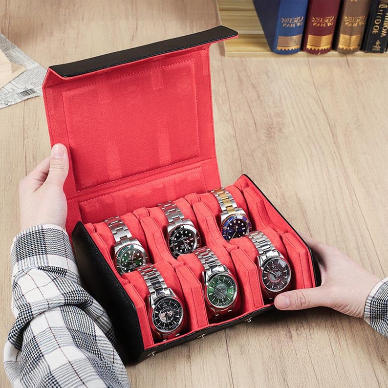 May include: A black and red watch case with six silver watches. The case is open, revealing a red interior with individual slots for each watch. The watches have various colored watch faces and silver bands. The case is held by a person.