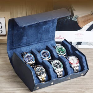 Może przedstawiać: Granatowe skórzane etui na zegarki z zamszowym wnętrzem, mieszczące siedem zegarków na rękę z tarczami w różnych kolorach i metalowymi paskami. Etui posiada zapięcie na klapę.