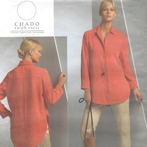 Pode incluir: Uma camisa de manga comprida cor coral com fecho de botões na frente e uma bainha ligeiramente curva. A camisa é mostrada em uma modelo usando calças bege.