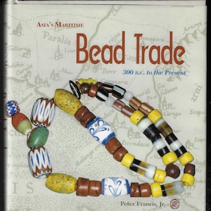 Puede incluir: La portada del libro "Bead Trade" con el subtítulo "300 a.C. to the Present". La portada presenta un fondo de mapa y un collar de cuentas de colores. Las cuentas son de varias formas y colores, incluyendo amarillo, azul, blanco y marrón.