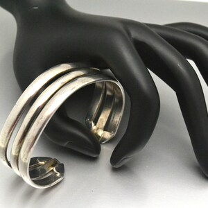 May include: A silver bangle bracelet with three bands. The bracelet is open and has a simple design.