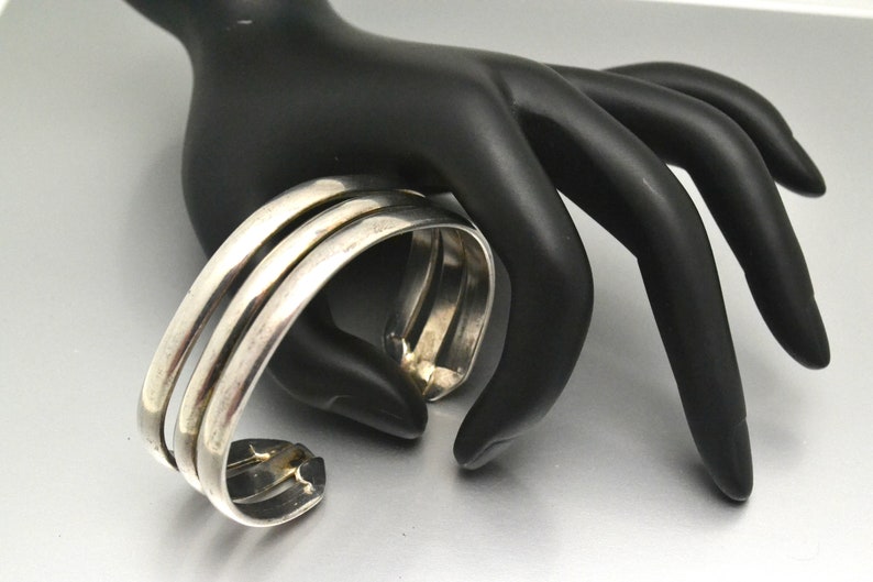 May include: A silver bangle bracelet with three bands. The bracelet is open and has a simple design.