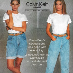 May include: An advertisement for Calvin Klein Jeans featuring two models wearing white t-shirts, denim shorts and jeans, and brown belts. The text reads "Calvin Klein's newest jeans look good with everything."