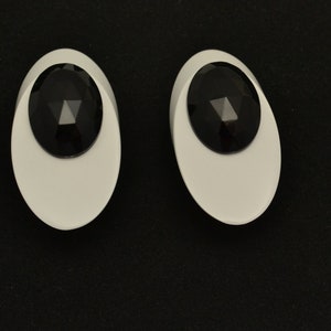 May include: A pair of white oval-shaped earrings with black faceted stones in the center.