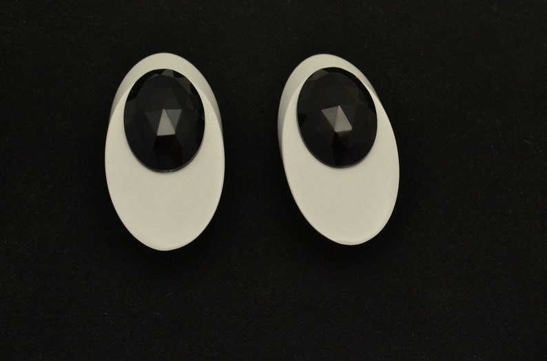 May include: A pair of white oval-shaped earrings with black faceted stones in the center.