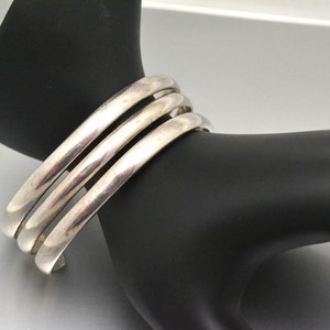 May include: Three silver bangle bracelets stacked on top of each other. The bracelets are smooth and shiny.