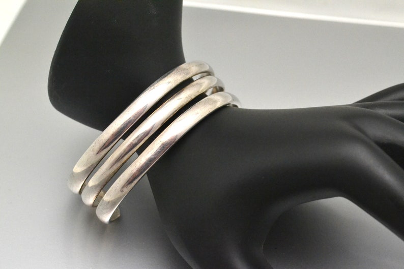 May include: Three silver bangle bracelets stacked on top of each other. The bracelets are smooth and shiny.