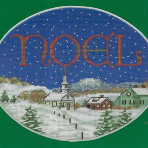 May include: A cross-stitch pattern featuring a winter scene with a church, houses, and trees. The sky is blue with white stars and the word "Noel" is stitched in red.