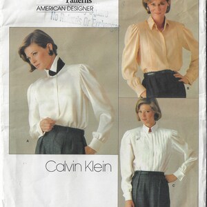 May include: A vintage sewing pattern for a white blouse with puffed sleeves. The pattern is by Vogue Patterns and designed by Calvin Klein. The pattern number is 1211.