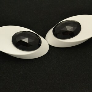 May include: A pair of white oval-shaped earrings with black faceted gemstones in the center.