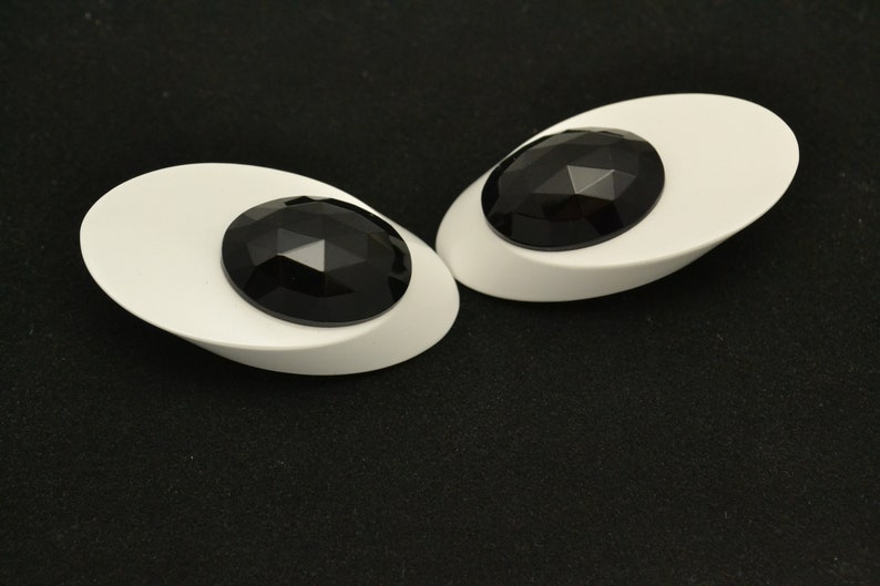 May include: A pair of white oval-shaped earrings with black faceted gemstones in the center.