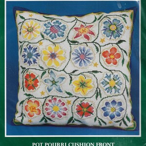 May include: A square, white cross-stitch pillow front with a floral design. The design features colorful flowers in shades of yellow, red, blue, and pink, connected by green vines. The text "POT POURRI CUSHION FRONT" is at the bottom.