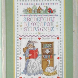 Puede incluir: Un patrón de punto de cruz con un alfabeto colorido, una mujer leyendo un libro y un ganso en un nido. El patrón está rodeado por un borde de corazones y las palabras "Mother Goose".