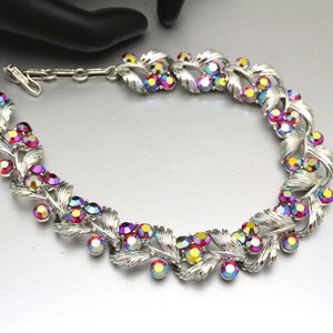 May include: A silver tone necklace with a delicate leaf design and iridescent red and pink rhinestones.