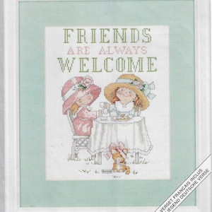 Puede incluir: Patrón de punto de cruz con dos chicas con vestidos y sombreros rosas tomando el té con un gato. El texto dice "Los amigos siempre son bienvenidos".