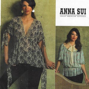 May include: Two women's tops with a floral pattern. The top on the left is black and white with a deep V-neck and long sleeves. The top on the right is light blue with a white bow and short sleeves. The text "ANNA SUI VOGUE' AMERICAN DESIGNER" is visible in the top right corner.