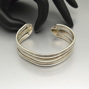 May include: A silver bangle bracelet with three bands. The bracelet is open and has a simple design.