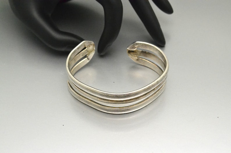 May include: A silver bangle bracelet with three bands. The bracelet is open and has a simple design.
