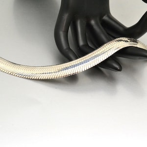Puede incluir: Un brazalete de cadena de serpiente de plata con un acabado pulido.