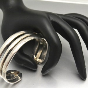 May include: A silver bangle bracelet with three bands. The bracelet is made of smooth, polished metal and has a simple, elegant design.