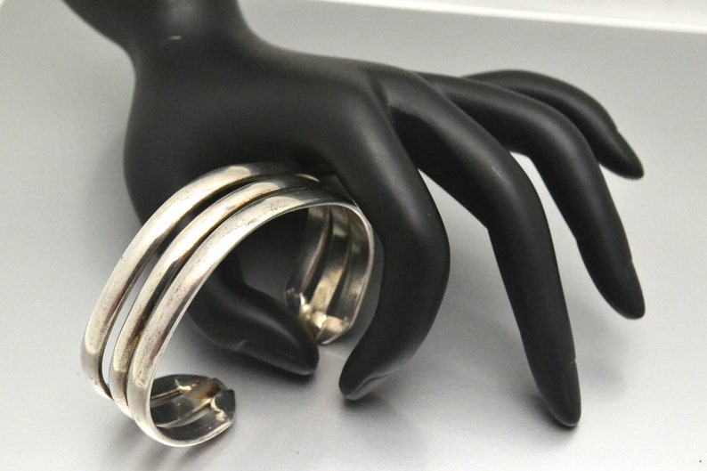 May include: A silver bangle bracelet with three bands. The bracelet is made of smooth, polished metal and has a simple, elegant design.