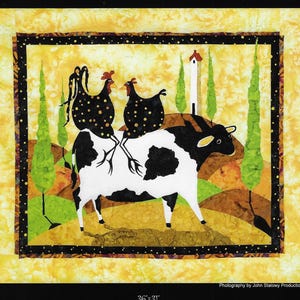 May include: A black and white cow with two black and white chickens perched on its back. The cow is standing on a brown and green hillside with a white building in the background. The image is framed with a black border and has a yellow background.