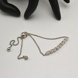 Op de afbeelding: Een verstelbare zilveren armband met een rij kleine, vierkante zirkonia-stenen.