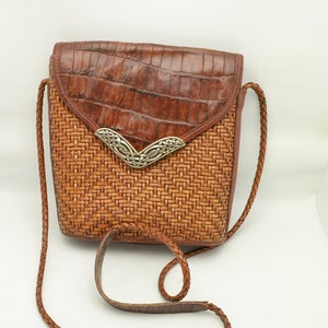 Puede incluir: Bolso bandolera marr&oacute;n con cuerpo tejido y solapa con estampado de cocodrilo. Cuenta con una correa trenzada y un cierre decorativo plateado. Ideal para llevar lo esencial.