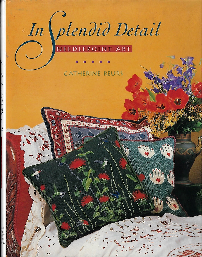 May include: A book titled "In Splendid Detail: Needlepoint Art" by Catherine Reurs, featuring a close-up of needlepoint pillows with floral and hummingbird designs.