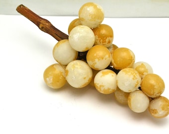 May include: A cluster of white and yellow alabaster grapes with a brown wooden stem.
