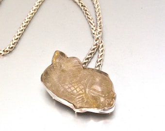 May include: A silver chain necklace with a clear quartz pendant carved in the shape of a fish.