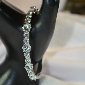 Puede incluir: Un brazalete de plata con una fila de piedras ovaladas de color azul claro.