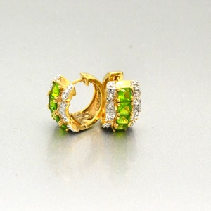 May include: A pair of gold hoop earrings with green and white gemstones. The earrings are made of gold and have a polished finish.