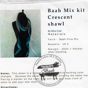 May include: A black mannequin displays a crescent shawl kit. The kit includes Baah Pixie Mix yarn, a US size 6 needle, and instructions. The shawl features teal, black, and gray color gradients. The text reads "Baah Mix kit Crescent shawl."