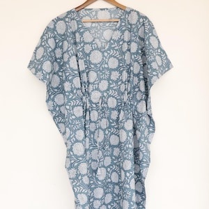 Peut inclure: Une robe caftan à imprimé floral bleu et blanc suspendue à un cintre en bois. La robe a un col en V et une taille à cordon. Le tissu est une matière douce et fluide, parfaite pour les journées chaudes.