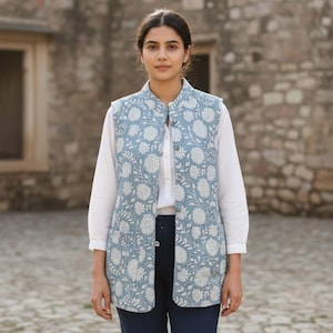 Puede incluir: Chaleco azul claro con estampado floral blanco, usado sobre una camisa blanca y combinado con pantalones azul marino. El chaleco tiene cuello mandarín y cierre de botones. Adecuado para ocasiones informales o semiformales.