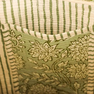 Pu&ograve; includere: Primo piano dell'interno di una borsa tote. La fodera presenta strisce verticali color crema e verdi. &Egrave; visibile una tasca, che mostra un motivo floreale in verde e bianco. Il design della borsa suggerisce un'estetica naturale.